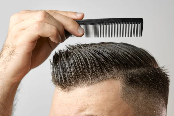 Fechar jovem penteando o cabelo com um pente de plástico. Cabelo de estilo após barbearia. — Fotografia de Stock