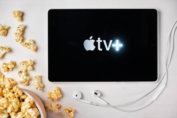 Apple tv plus Logo auf dem Bildschirm des Tablets, das auf dem weißen Tisch liegt und mit Popcorn bestreut ist. August 2020, San Francisco, USA — Stockfoto