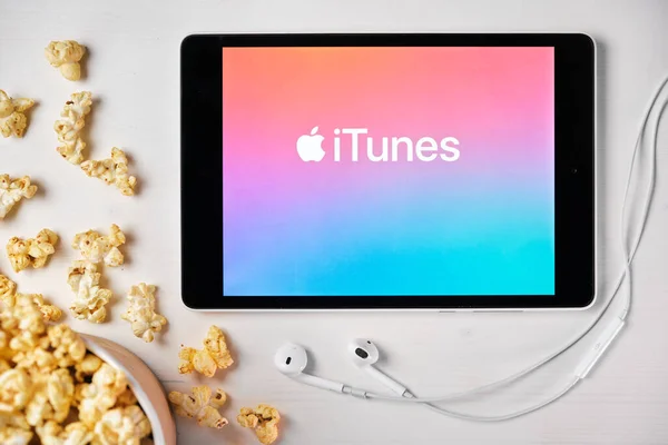 Logotipo de iTunes en la pantalla de la tableta colocada en la mesa blanca y espolvoreado palomitas de maíz en ella. Auriculares Apple cerca de la tableta, agosto 2020, San Francisco, EE.UU. — Foto de Stock