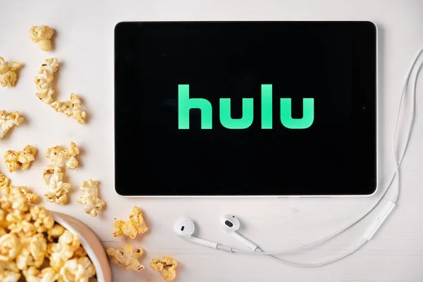 Hulu logo on the screen of the tablet laying on the white table and sprinkled popcorn on it. Apple earphones near the tablet, August 2020, San Francisco, USA — Stock Photo, Image