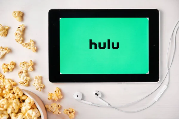 Hulu logo on the screen of the tablet laying on the white table and sprinkled popcorn on it. Apple earphones near the tablet, August 2020, San Francisco, USA — Stock Photo, Image