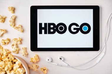 Beyaz masada duran tabletin ekranında HBO GO logosu ve üzerine patlamış mısır serpiştirilmiş. Tabletin yanındaki Apple kulaklıklar, Ağustos 2020, San Francisco, ABD