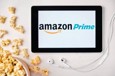 Tabletin ekranındaki Amazon ana video logosu beyaz masaya serpilmiş ve üzerine patlamış mısır serpiştirilmiş. Tabletin yanındaki Apple kulaklıklar, Ağustos 2020, San Francisco, ABD