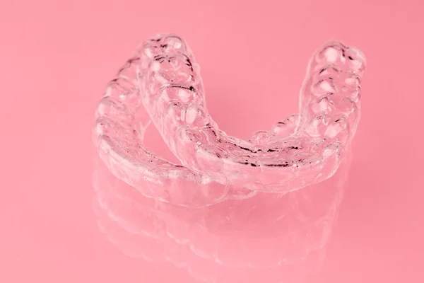 Dwa niewidoczne wyrównujące zęby na różowym tle. Ortodontyczne tymczasowe zdejmowane aparaty ortodontyczne do mocowania zębów po ustawieniu. Terapia po nawiasach. — Zdjęcie stockowe