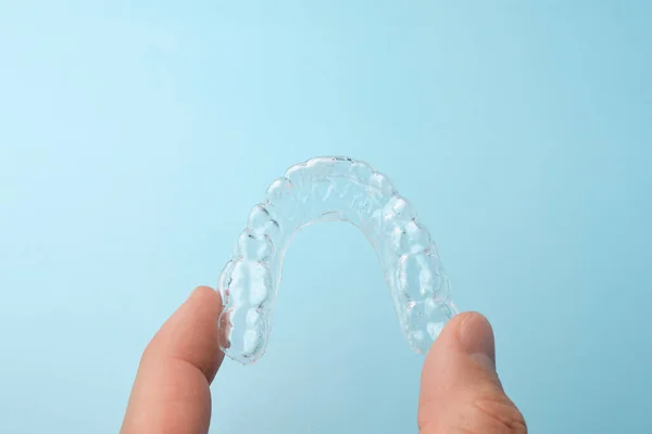 Κοντινό πλάνο mans χέρι κρατώντας ένα διαφανές αφαιρούμενο τιράντες για λεύκανση των δοντιών σε ένα μπλε φόντο με αντίγραφο χώρο. Αόρατοι οδοντίατροι για ίσιωμα δοντιών. — Φωτογραφία Αρχείου