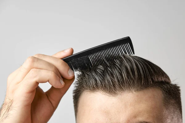 用塑料梳子把年轻人的头发梳得紧紧的.理发店之后的发型。头发保健。脱发概念 — 图库照片
