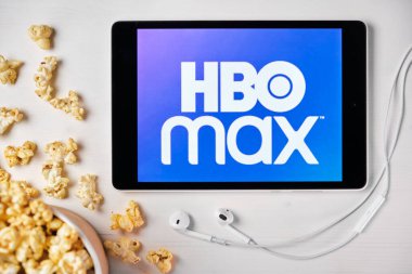 Beyaz masada duran tabletin ekranında HBO MAX logosu ve üzerine patlamış mısır serpiştirilmiş. Tabletin yanındaki Apple kulaklıklar, Ağustos 2020, San Francisco, ABD