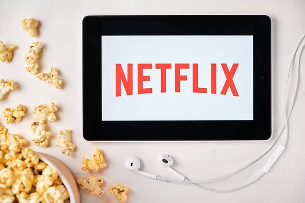 Логотип Netflix на экране планшета, лежащего на белом столе и посыпанного попкорном. Наушники Apple у планшета, показывающего приложение Netflix, август 2020 года, Сан-Франциско, США — стоковое фото