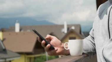 Adam akıllı telefonunu dağların ve yeni evlerin arka planında kullanıyor..