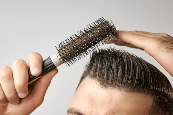 Een man die een ronde borstel gebruikt om zijn haar te stylen. Haarverzorging thuis na de kapper. Kammen van kort bruin haar op de witte achtergrond — Stockfoto