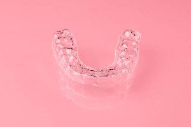 Pembe arka plandaki alt dişler için görünmez hizalayıcı ya da diş koruyucusu. Dişleri düzelttikten sonra ortodonti tedavisi.