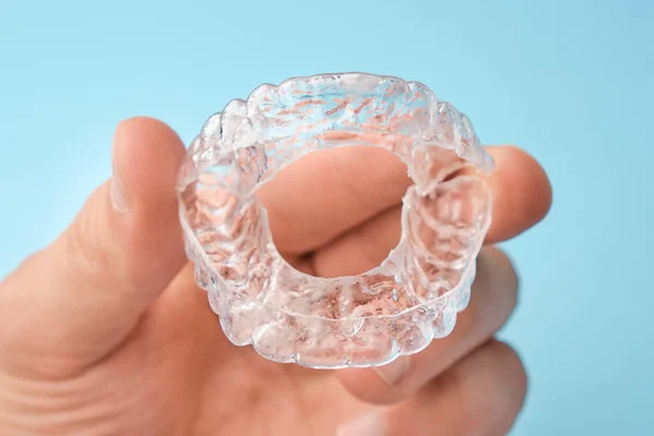 Κοντινό πλάνο mans χέρι κρατώντας αόρατο aligners για λεύκανση και ίσιωμα των δοντιών στο μπλε φόντο. Ορθοδοντική θεραπεία μετά από παρένθεση. Υγεία δοντιών — Φωτογραφία Αρχείου