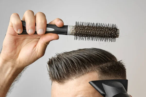 Hombre peinando su cabello con secador de pelo y cepillo redondo. Cuidado del cabello en casa después de la peluquería. Moda masculina y corte de pelo moderno. —  Fotos de Stock