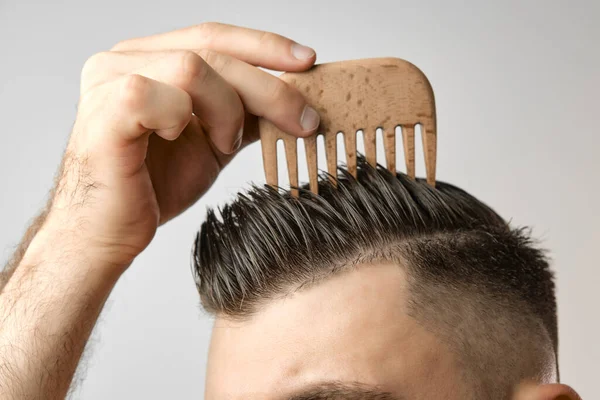 Close up man brushing his hair with wooden comb on the grey background. Treatment against hair lost and dandruff concept. Cosmetic products for men. Barbershop advertising. — Stock Photo, Image