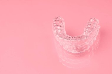 Pembe arka plandaki alt dişler için görünmez hizalayıcı ya da diş koruyucusu. Dişleri düzelttikten sonra ortodonti tedavisi.