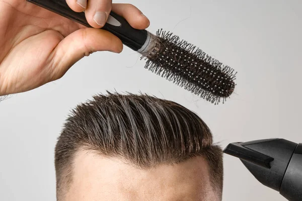Чоловік стилізує волосся з фен і круглою щіткою. Догляд за волоссям вдома після перукарні. Чоловіча мода і сучасна стрижка . — стокове фото