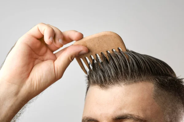 Großaufnahme Mann streicht sich die Haare mit Holzkamm auf dem grauen Hintergrund. Behandlung gegen Haarausfall und Schuppen Konzept. Kosmetische Produkte für Männer. Friseurwerbung. — Stockfoto