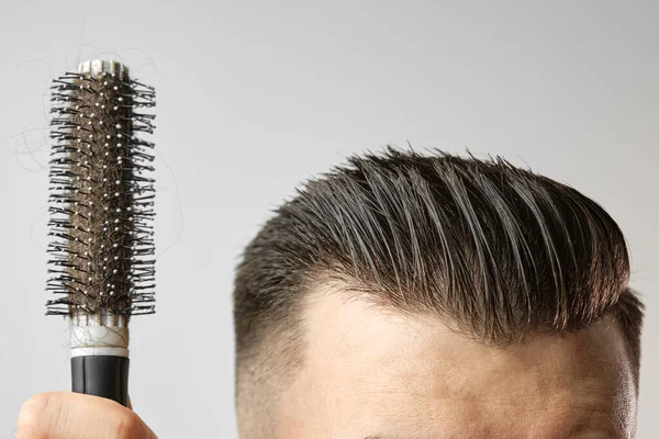 Homem usando uma escova redonda para estilizar seu cabelo. Cuidados com o cabelo em casa depois da barbearia. Pentear de cabelos castanhos curtos no fundo branco — Fotografia de Stock
