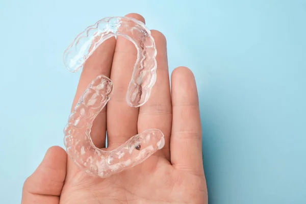 Feche os homens mão segurando alinhadores invisíveis para clareamento e alisamento dos dentes no fundo azul. Terapia ortodôntica após braquetes. Dentes cuidados de saúde — Fotografia de Stock