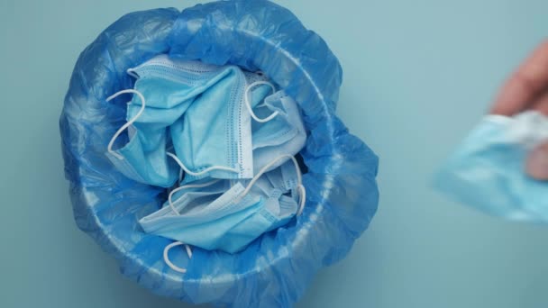 Mann wirft Maske in den Müll Ausrangierte Operationsmasken. Medizinische Abfälle auf blauem Hintergrund. — Stockvideo