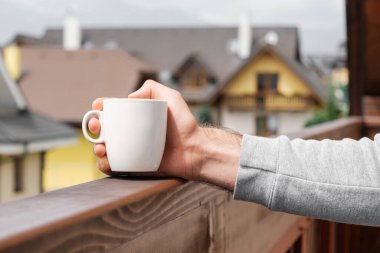 Modern evlerin arka planında beyaz bir bardak tutan adam..