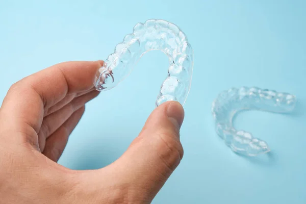 Feche os homens mão segurando alinhadores invisíveis para clareamento e alisamento dos dentes no fundo azul. Terapia ortodôntica após braquetes. Dentes cuidados de saúde — Fotografia de Stock