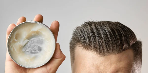 Mann, der Ton, Pomade, Wachs, Gel oder Mousse aus einer runden Metallbox aufträgt, um seine Haare nach dem Friseurhaarschnitt zu stylen. Werbekonzept für seine Produkte. Behandlung und Pflege gegen Haarausfall — Stockfoto