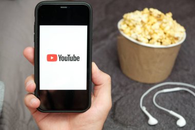 Yanında Apple kulaklıkları ve patlamış mısır kutusu olan XXX logolu bir cep telefonu taşıyan bir adamın elini kapat, Ağustos 2020, San Francisco, ABD