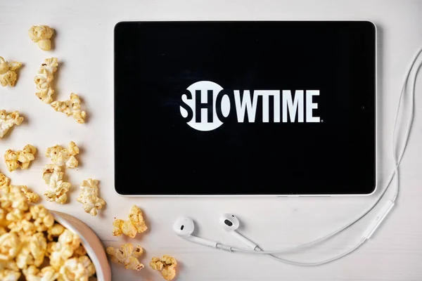 Logotipo Showtime en la pantalla de la tableta colocada en la mesa blanca con palomitas de maíz dispersas y auriculares Apple. Pasando tiempo libre en casa o anuncio de noticias, septiembre 2020, San Francisco, EE.UU.. —  Fotos de Stock