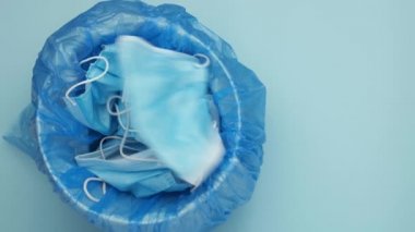 Adam çöp kutusuna maske atıyor. Atılmış cerrahi maskeler. Mavi arka planda tıbbi atık.