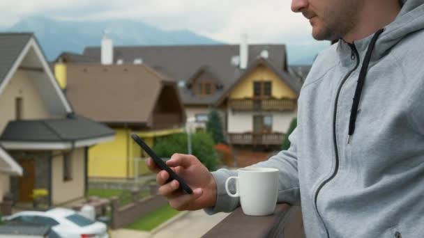 Homme utilisant son smartphone sur le fond des montagnes et des maisons neuves. Le matin parfait — Video