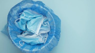 Adam çöp kutusuna maske atıyor. Atılmış cerrahi maskeler. Mavi arka planda tıbbi atık.