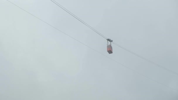 Elevador de esqui vermelho ou funicular se movendo ao longo do teleférico em nuvens do pico das montanhas — Vídeo de Stock