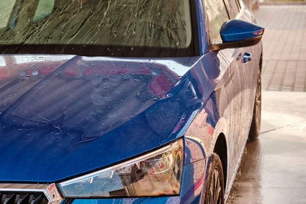 Feche o capô e o farol de um carro azul em uma gotas de água após a lavagem do carro. Carro limpo após lavagem de água de alta pressão. — Fotografia de Stock