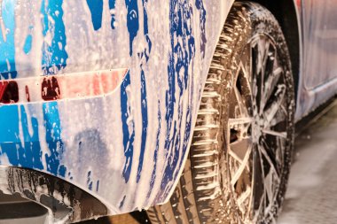 Yüksek basınç altında köpükle yıkanan mavi bir arabanın tekerleğini kapat. El işi oto yıkama konsepti. 