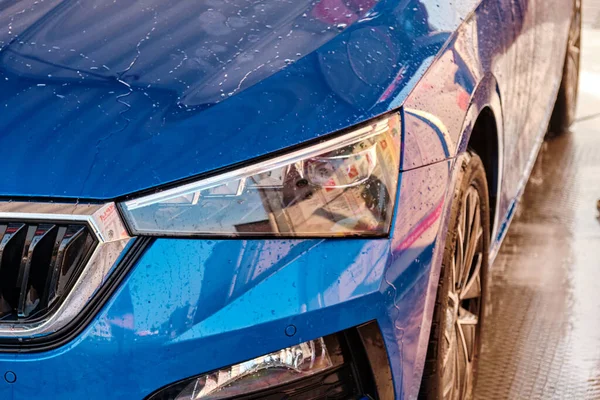 Feche o capô e o farol de um carro azul em uma gotas de água após a lavagem do carro. Carro limpo após lavagem de água de alta pressão. — Fotografia de Stock