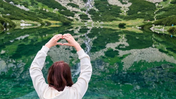 Закройте женские руки, показывающие сердце на удивительном фоне водопада и прозрачной, чистой воды озера с копировальным пространством. Концепция призвания в горах. Одиночество с природой. — стоковое фото