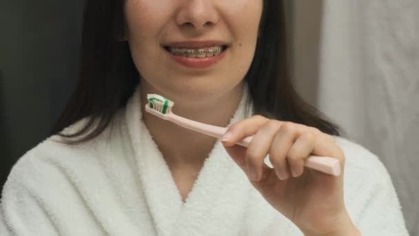 Bilder på hur man rengör tänder korrekt med hängslen av kvinna i vit badrock i spegelreflektion — Stockvideo