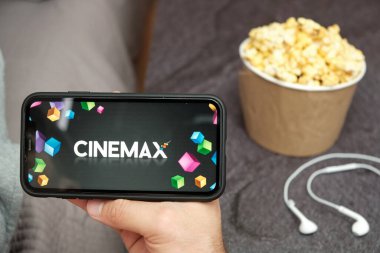 Mobil telefon ekranında Cinemax logosu, arka planda patlamış mısır kutusu ve Apple kulaklıkları, Eylül 2020, San Francisco, ABD