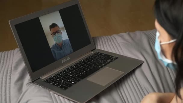 Mujer acostada en la cama y teniendo una conferencia en línea con un hombre con una posible máscara. Oficina del hogar durante la pandemia de coronavirus. junio 2020, Praga, República Checa. — Vídeo de stock