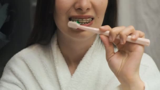 Záběry, jak správně čistit zuby rovnátka od ženy v bílém županu v zrcadlovém odlesku — Stock video