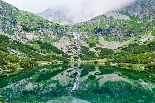 Panoramiczny widok na wodospad i jezioro z przezroczystą wodą w pobliżu Sliezsky House. Odbicie krajobrazu lądowego w wodzie jeziora Velicke Mountain. Pocztówka. — Zdjęcie stockowe