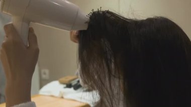 Saç kurutma makinesi ve banyoda yuvarlak fırçayla saçını kurutan bir kadın..