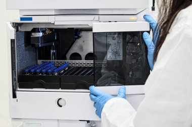 Bilim adamı numuneyi HPLC sistemindeki otomatik örnekleme rafına mavi kapaklı cam bir şişe içine koydu. Ayrıştırma bileşikleri için yüksek performanslı sıvı kromatografi. Koronavirüs ve ilaçlara karşı aşının geliştirilmesi.