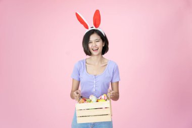 Paskalya Yumurtası Festivali 'nde parlak pembe arka planda güzel bir Asyalı kadın. Paskalya Tavşanı kostümlü kadın elinde renkli Paskalya yumurtaları tutuyor. Güzel kadın portresi. Yakından..