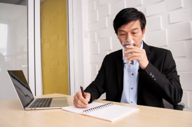 Asyalı yaşlı işadamı uzun süre çalıştıktan sonra mola veriyor. Bir adam cam portrede soğuk su içiyor ve fotokopi çekiyor..