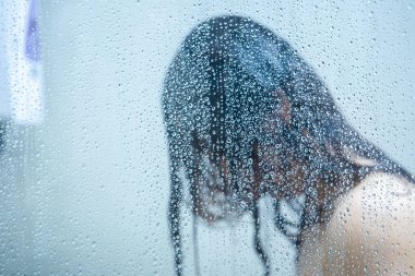 Güzel bir Asyalı kadın, duş odasında bir damla su ve cam üzerinde duş almaktan zevk alır..