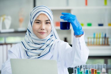 Asyalı genç Müslüman bilim adamı hastane laboratuvarında kimyasal deneyi test ediyor. Laboratuvarda araştırma yapan ve deney yapan profesyonel bir kimyager..
