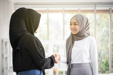 Güzel Asyalı Müslüman iş kadını meslektaşıyla tokalaşıyor. Yakın plan..