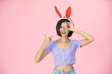 Paskalya Yumurtası Festivali 'nde parlak pembe arka planda güzel bir Asyalı kadın. Paskalya Tavşanı kostümlü kadın elinde renkli Paskalya yumurtaları tutuyor. Güzel kadın portresi. Yakından..